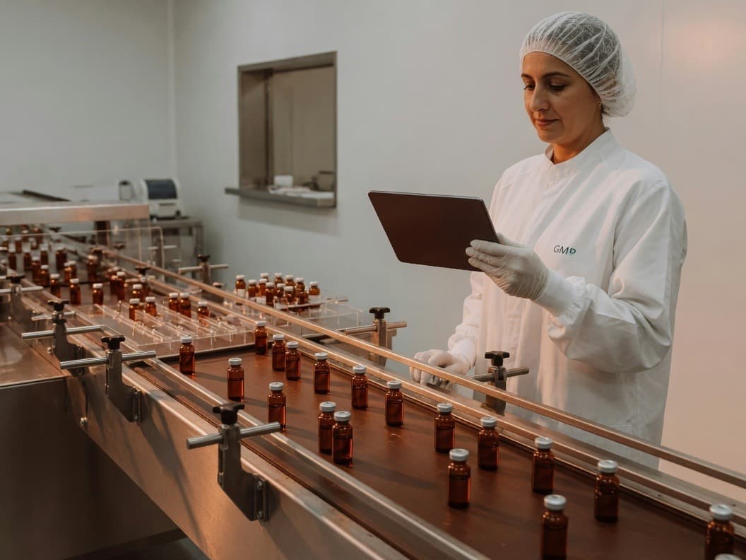 Quality professional reviewing a digital record beside a fill-finish line of amber vials